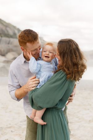 A joyful family moment captured on a beach with mountains in the background.