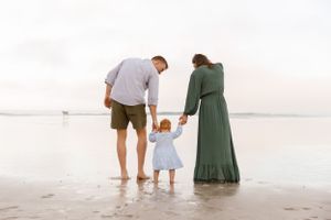 A family holding hands while standing in the shallow waters of a beach at sunset.