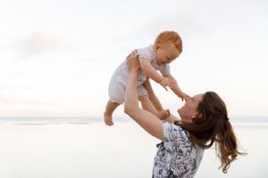 A joyful moment between parent and baby playing together on a sunlit beach at sunset.