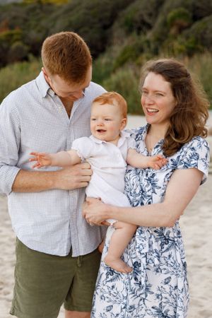 A young family shares a joyful moment together outdoors, with their smiling baby wearing white.