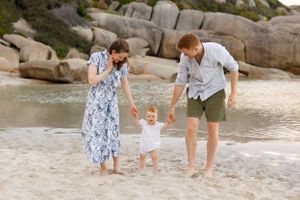 Three people enjoy a beach day together strolling through shallow water near rocky coastal boulders.