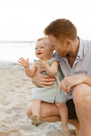 A joyful moment shared between parent and baby playing together on a sandy beach at sunset.