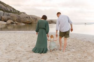Family walking together on a scenic beach with rocky cliffs, wearing a green dress and casual attire.