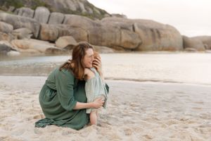 A candid family moment captured on a beach with rocky outcrops in the background.