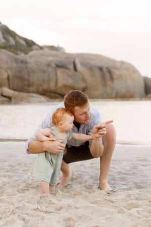 A heartwarming beach scene as a parent points something out to a toddler on the sandy shore.