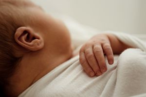 A series of close-up photos showing a newborn baby's hands, feet, and face wrapped in soft white blankets.