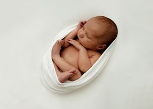 A sleeping newborn baby curled up peacefully in a white oval-shaped bowl during a professional photo session.