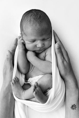 Black and white artistic series showing a sleeping newborn cradled in gentle hands against white fabric.