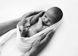 Black and white artistic photographs show a newborn baby wrapped in soft white fabric in various gentle poses.