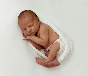 A sleeping newborn baby wrapped in soft white fabric lies peacefully against a light neutral background.