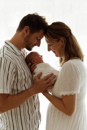 A series of intimate maternity photos showing a couple in white embracing a pregnant belly against a bright background.