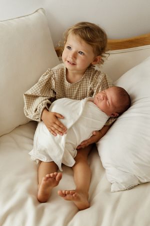 A series of tender moments captured in soft, natural light showing siblings bonding on white bedding.