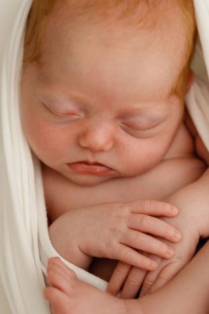 Peaceful sleeping newborn baby wrapped in soft white fabric, with tiny hands crossed.