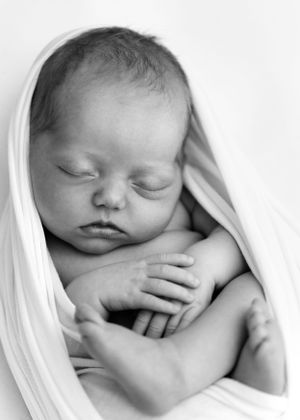 A peaceful black and white portrait of a sleeping newborn baby wrapped in soft white fabric.