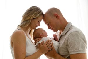 Parents lovingly hold their newborn baby against a soft white backdrop in tender family moment.