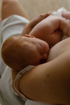 Intimate close-up of newborn baby nursing while tenderly cradled against mother's chest in soft natural light.