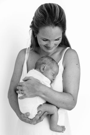 A tender black and white portrait showing a mother in white smiling down at her sleeping newborn baby.