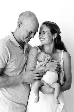 A heartwarming black and white portrait of parents sharing a tender moment with their sleeping newborn baby.