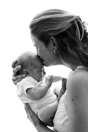A heartwarming black and white photograph of a tender moment between a mother and baby in soft natural light.