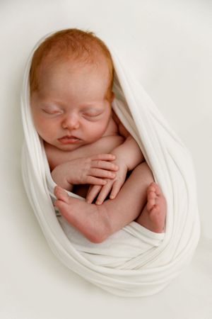 Peaceful sleeping newborn baby wrapped in soft white fabric against white background.