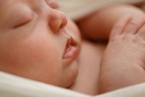 Close-up view of a sleeping newborn baby's peaceful face resting on soft white fabric.