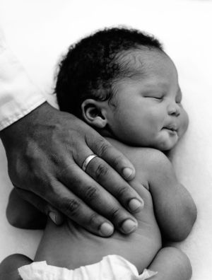 A tender black and white photograph shows a caring hand gently resting on a sleeping baby's bare shoulder.