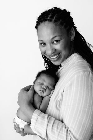 Black and white portrait of a parent lovingly holding a sleeping newborn baby against their white shirt.