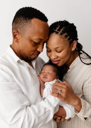 A tender family moment as parents lovingly embrace their sleeping newborn baby swaddled in white.