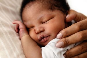 A peaceful sleeping newborn baby nestled in soft white bedding with gentle hands offering comfort.