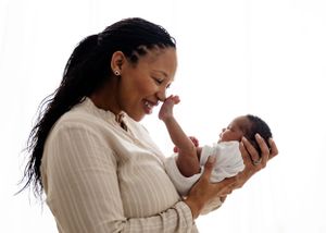 Mother in white sweater joyfully interacting with her tiny infant in a heartwarming moment against white background.