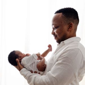 A joyful moment between parent and baby wearing white, captured against a minimalist white background.