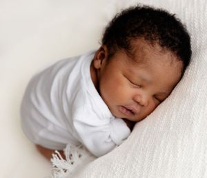 Peaceful sleeping newborn baby in white clothing rests on soft white fabric.