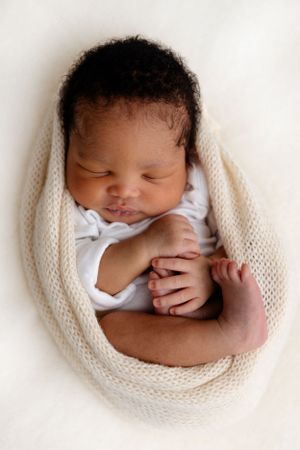 A sleeping newborn baby swaddled in a soft white knit blanket while taking their first photos.