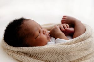 Peaceful sleeping newborn wrapped in soft knitted white blanket.