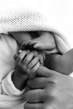 Close-up black and white image of tiny baby hands being tenderly held in an adult's grasp under soft knit blanket.