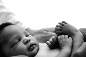 Black and white portrait of a baby lying down with tiny feet curled up in a peaceful pose.