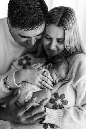 Black and white photo of parents lovingly cradling their sleeping newborn baby together.