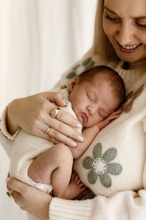 Smiling mother in floral sweater gently holds sleeping newborn baby against her chest.