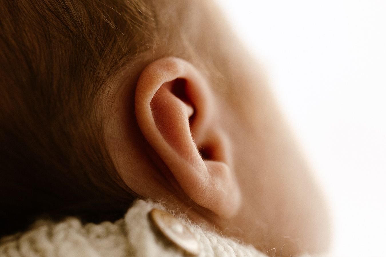 Close-up of a newborn baby's delicate ear, showcasing soft skin and tiny ear details in warm, natural light.