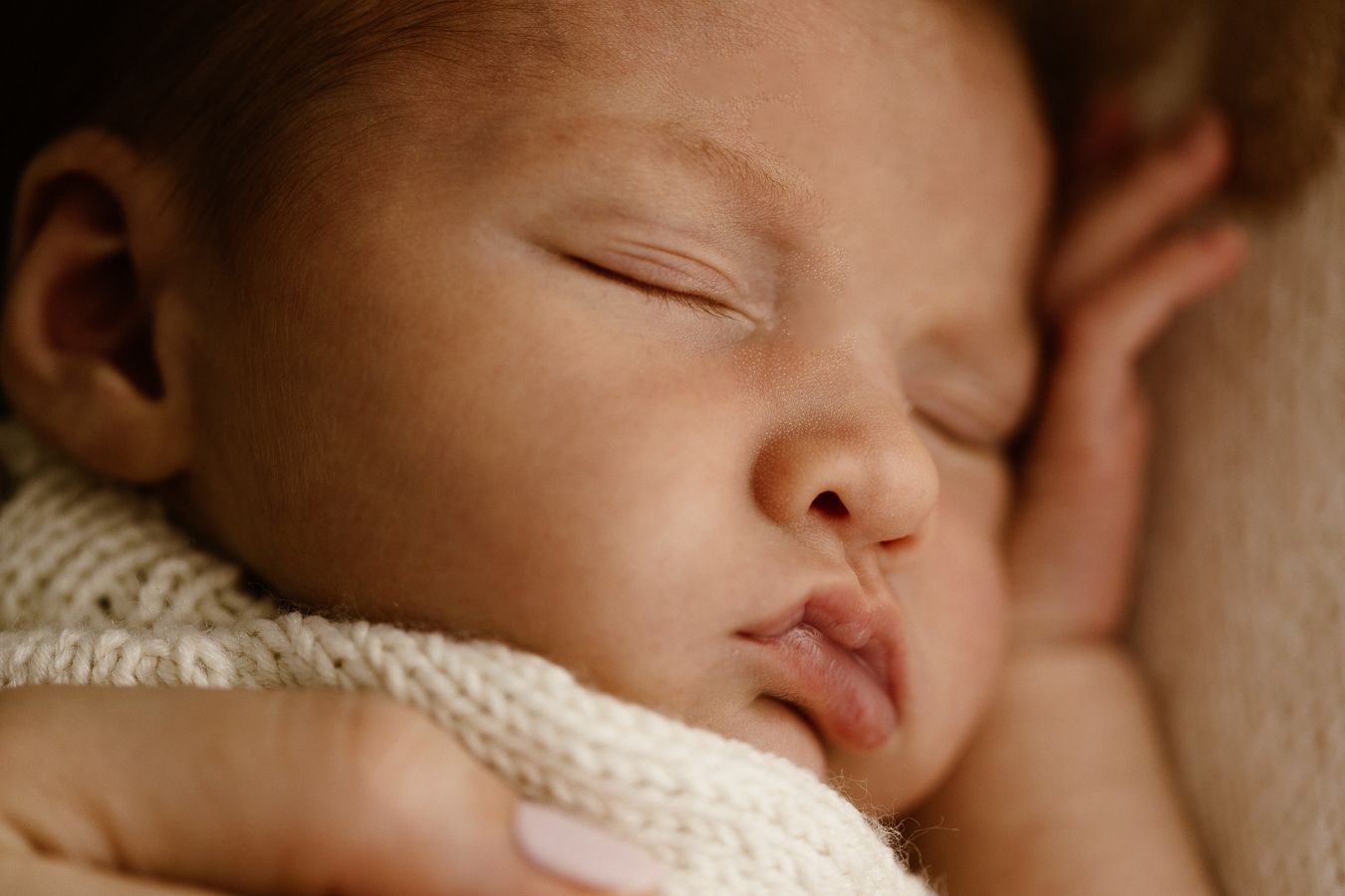 Close-up of a peacefully sleeping newborn baby wrapped in a soft cream knit blanket.