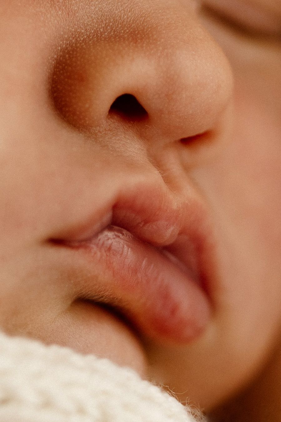 Close-up macro photo of a newborn baby's nose and lips, showing delicate soft skin and tiny facial features.