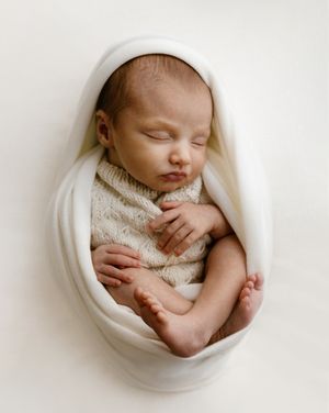 Peaceful newborn baby sleeping wrapped in a soft white knit blanket, curled in a cozy pose.
