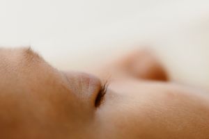 Close-up macro photo of a sleeping baby's closed eye with delicate eyelashes on soft skin.