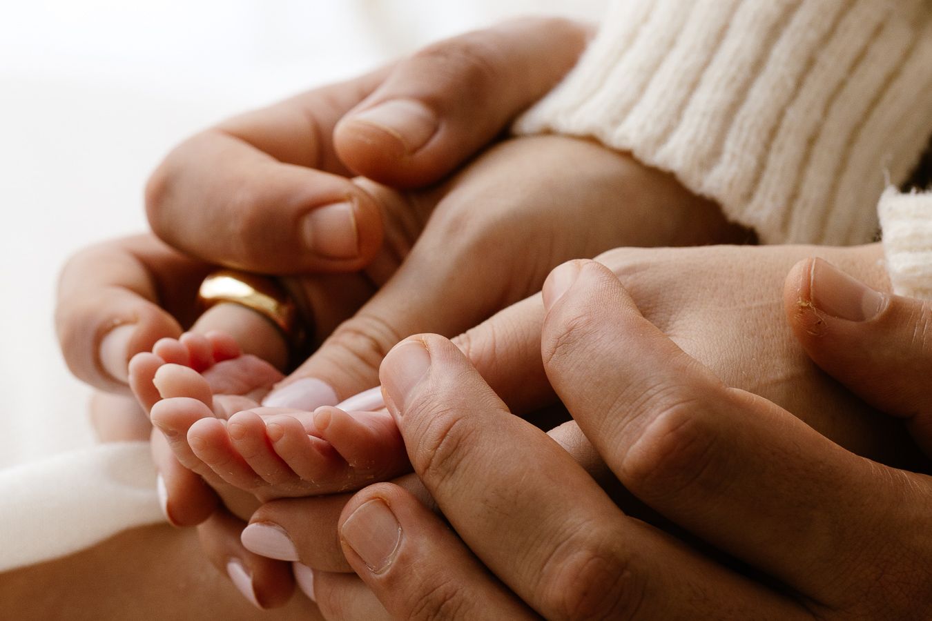 Adult hands gently cradling a newborn baby's tiny feet, symbolizing family love and new parenthood.