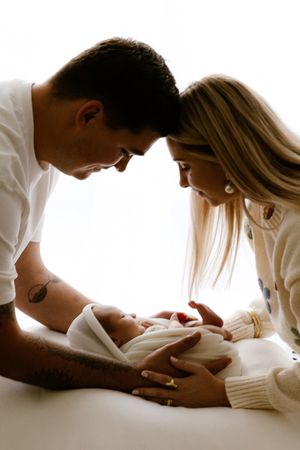 A couple lovingly gazes at their newborn baby wrapped in white, sharing a tender family moment together.