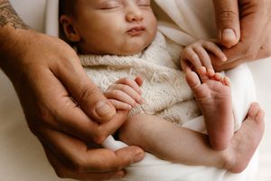 Sleeping newborn baby held gently by parents hands, wearing a knit sweater, in a soft white blanket.
