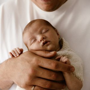 A peaceful newborn baby sleeping soundly in the loving arms of a parent wearing a white shirt.