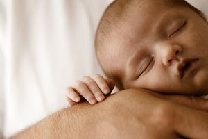 Peaceful newborn baby sleeping on parent's arm, eyes closed, tiny fingers curled gently.