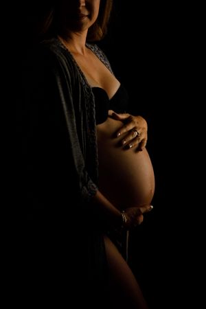 A dramatic black and white maternity photo showing a pregnant belly silhouetted against dark lighting.