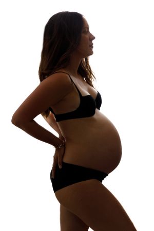 Silhouetted profile of pregnant woman in black lingerie against white background showing maternity curves.